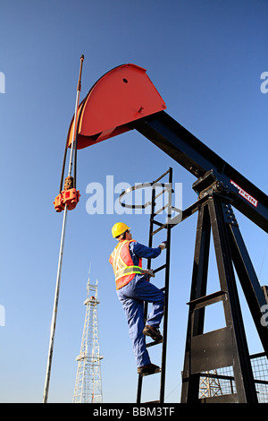 Worker climbing pump jack avec de l'huile de forage en arrière-plan à découvrir du pétrole canadien Museum de Devon, en Alberta Canada Banque D'Images