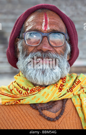 Le portrait d'un vieux mendiant indien homme à barbe grise, grandes, épaisses lunettes cerclées et un accueil chaleureux hat marron, Varanasi, Inde Banque D'Images