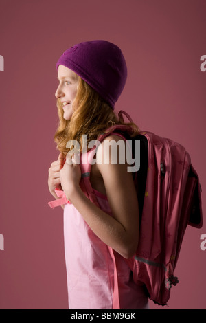 Fille aux cheveux roux portant un bonnet violet et une besace sac en face d'une toile rose Banque D'Images