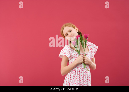 Fille aux cheveux roux avec des tresses, portant une robe d'été en face d'une toile rouge avec des fleurs Banque D'Images