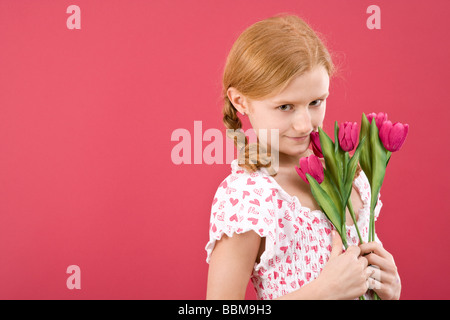 Fille aux cheveux roux avec des tresses, portant une robe d'été en face d'une toile rouge avec des fleurs Banque D'Images