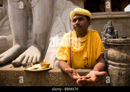 Un prêtre se tient au pied de la statue de Lord Bahubali à Shravanabelagola, Karnataka, Inde. Banque D'Images