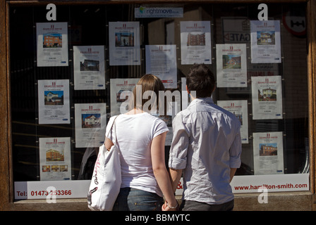 Jeune couple à la recherche de maisons à vendre à une fenêtre d'agents immobiliers Banque D'Images