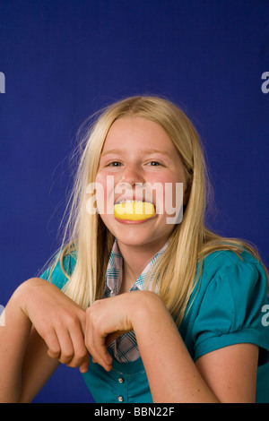 Portrait de jeune fille 10-12 ans holding sour lemon dans les dents de la bouche, studio shot cut out MR ©Pearson Myrleen Banque D'Images