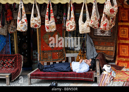 Un jeune homme se trouve confortablement sur un tapis sur un banc en face de sa boutique, à l'aide d'un téléphone mobile, Bazar, Sultanahmet, Istanbul, Banque D'Images