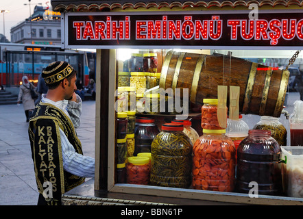 Vendeur de rue en uniforme historique à côté d'une voiture avec des légumes marinés, soir, Eminoenue, Istanbul, Turquie Banque D'Images