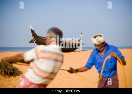 Christian indien tirant dans les filets des pêcheurs sur la plage avec un bateau en bois traditionnel fabriqué à la main en arrière-plan. Banque D'Images