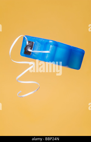 Distributeur de fil dentaire en plastique bleu avec le curling longueur de fil dentaire hanging out. Isolé sur fond jaune Banque D'Images