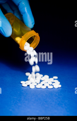 Close-up d'une main dans un gant chirurgical bleu vidage une prescription d'orange bouteille de pilules blanches Banque D'Images