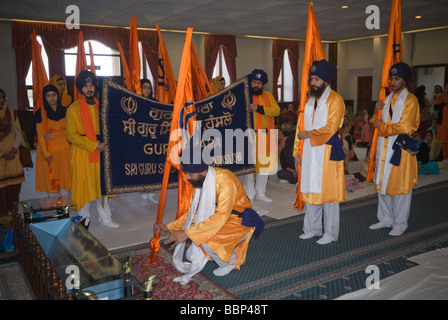 Les Sikhs dans la salle de culte a Hounslow Gurdwara pour célébrations du Vaisakhi . Hommes portant des drapeaux Sikh arc à la Guru Granth Sahib Banque D'Images