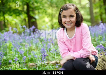 Jeune fille assise dans un bois plein de bluebells Banque D'Images