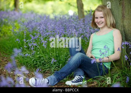 Jeune fille assise contre un arbre dans un bois plein de bluebells Banque D'Images