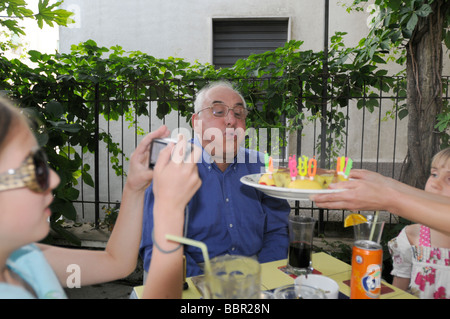 Un grand-père célèbre son 70e anniversaire avec un gâteau d'anniversaire surprise. Banque D'Images