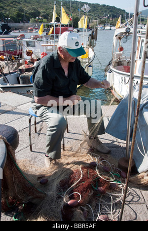 Un pêcheur réparant ses filets dans le port de Talamone dans la Maremma, en Toscane Banque D'Images