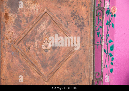 Un rusty metal gate est encastré dans un mur mauve décoré à la main dans la région de Carrizozo, Nouveau Mexique. Banque D'Images