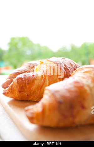 Croissants fraîchement cuits sur une planche de bois, avec un fond de jardin flou, capturant l'essence d'un petit déjeuner détendu et invitant Banque D'Images