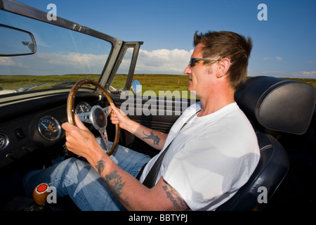 L'homme tatoué dans son mi-quarantaine bénéficiant au volant d'une voiture classique convertible Banque D'Images