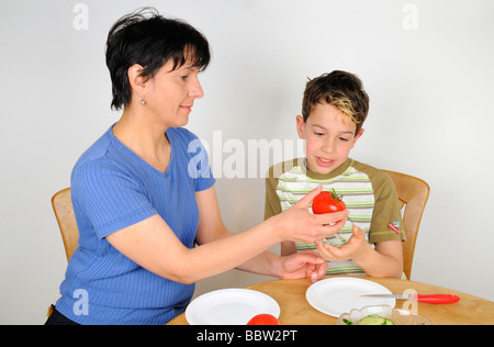 Femme donnant un garçon une tomate à couper pour une salade Banque D'Images