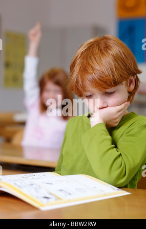 Les enfants dans une salle de classe à l'école primaire, rêvasser ou garçon à pas sûr, pensif, triste ou frustré, les garçons de devenir le Banque D'Images