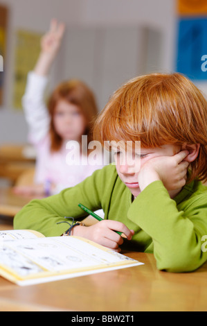 Les enfants dans une salle de classe à l'école primaire, rêvasser ou garçon à pas sûr, pensif, triste ou frustré, les garçons de devenir le Banque D'Images