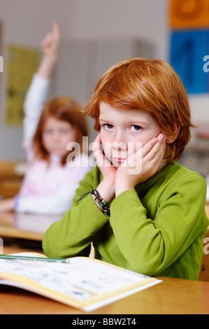 Les enfants dans une salle de classe à l'école primaire, rêvasser ou garçon à pas sûr, pensif, triste ou frustré, les garçons de devenir le Banque D'Images