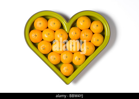 Fruit vert en forme de coeur bol plein d'oranges Banque D'Images