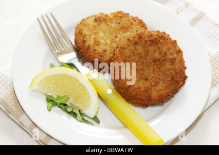 La morue panés délicieux fraîchement préparés Fishcakes avec citron et garnir de feuilles de salade isolé sur un fond blanc avec aucun peuple et un chemin de détourage Banque D'Images