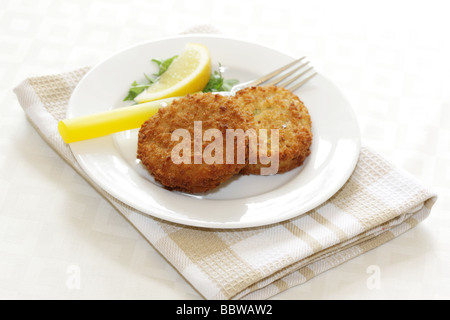 La morue panés délicieux fraîchement préparés Fishcakes avec citron et garnir de feuilles de salade isolé sur un fond blanc avec aucun peuple et un chemin de détourage Banque D'Images