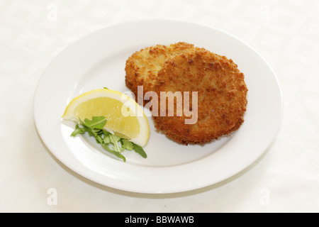 La morue panés délicieux fraîchement préparés Fishcakes avec citron et garnir de feuilles de salade isolé sur un fond blanc avec aucun peuple et un chemin de détourage Banque D'Images