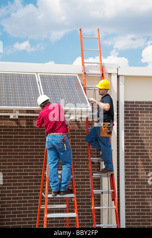 Deux travailleurs de l'installation de panneaux solaires sur le côté d'un bâtiment vertical avec place pour le texte Banque D'Images