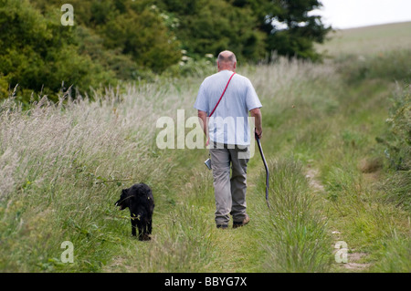Un homme promenait son chien le long d'une voie de pays au bord d'un champ Banque D'Images