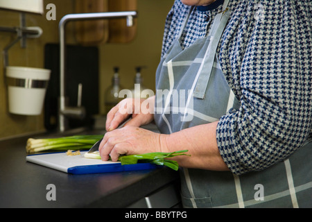 Mains de femme, 67 ans, coupe oignons de printemps dans la cuisine Banque D'Images