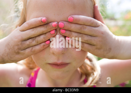 Girl holding hands jusqu'à son visage, couvrant ses yeux, avec du vernis à ongle rose et les mains sales Banque D'Images