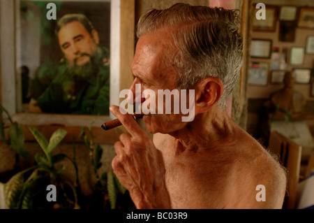 Un ancien révolutionnaire fume un cigare devant une affiche de Castro à La Havane, Cuba. Banque D'Images