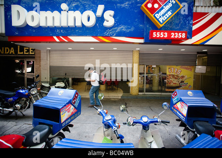 Un homme marche dans la rue entre certains garé les motos et un restaurant Pizza fermé dans la ville de Mexico, DF, Mexique. Banque D'Images