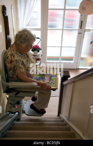 Une vieille dame utilise un télésiège pour monter et descendre les escaliers dans sa maison avec son petit-déjeuner Banque D'Images