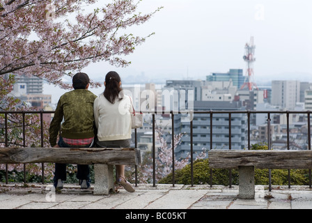 Couple dans l'amour est assis sur le banc d'un parc surplombant la ville d'Otsu dans la préfecture de Shiga, au plus fort de la saison des cerisiers en fleur Banque D'Images