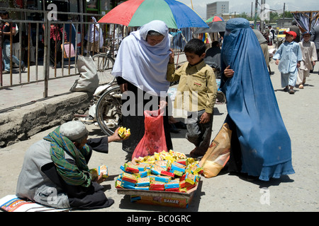 Dans une rue de Kaboul deux femmes et un jeune garçon à envisager l'achat d'un paquet de biscuits d'un vendeur de rue Banque D'Images