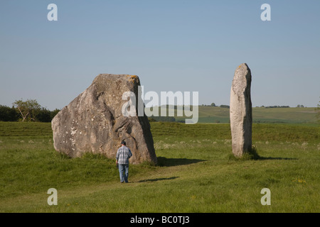 Homme marchant devant deux énormes pierres à Avebury Stone Circle dans le Wiltshire sur une journée ensoleillée Banque D'Images