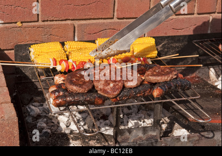 Close-up de saucisses, des hamburgers et du maïs et des kebabs par cuisson à l'extérieur à l'air libre sur un barbecue (BBQ) à l'été Banque D'Images