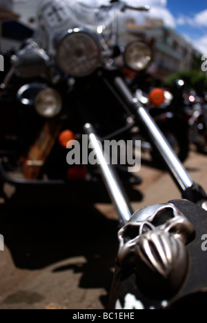 Un crâne orne la roue avant d'une moto. Gros plan du guidon de moto personnalisé avec ornement de crâne chromé et pièces de moteur floues. Banque D'Images