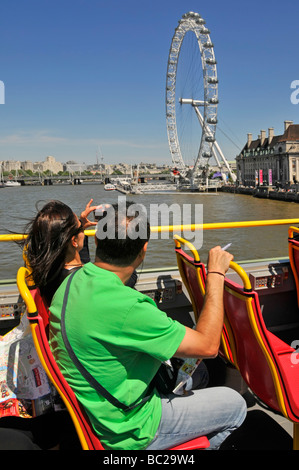 Pont supérieur jour de ciel bleu ensoleillé sur un bus touristique à toit ouvert couple prenant des photos de la Tamise et de la grande roue London Eye Angleterre Royaume-Uni Banque D'Images