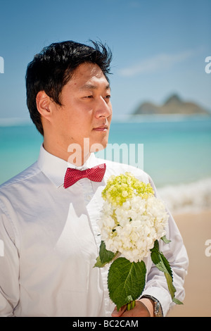 Asian groom attend patiemment son épouse avec un bouquet de fleurs sur la plage Lanikai, Kailua, Hawaii. Banque D'Images
