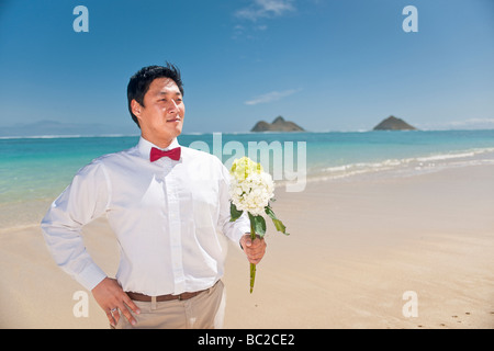 Asian groom attend patiemment son épouse avec un bouquet de fleurs sur la plage Lanikai, Kailua, Hawaii. Banque D'Images
