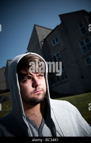 Jeune homme portant un sweat à l'extérieur un bloc d'appartements, seul l'air préoccupé pensif Banque D'Images