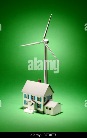 Une petite éolienne de métal sur un fond vert avec une petite maison Banque D'Images