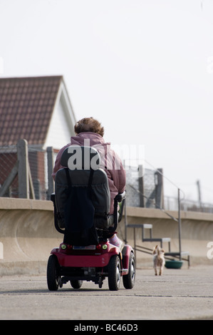 Dame âgée à l'aide d'un scooter de mobilité le long d'une promenade au bord de la mer en Angleterre Banque D'Images