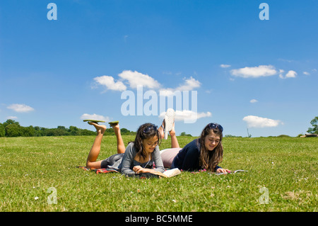 Portrait horizontal de deux jeunes filles couché dans l'herbe la lecture de livres et l'écoute d'un ipod sur une journée ensoleillée Banque D'Images