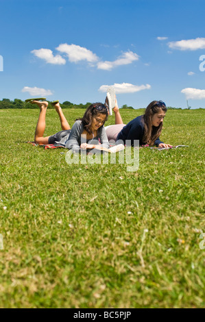 Portrait vertical de deux jeunes adolescentes couché dans l'herbe la lecture de livres et l'écoute d'un ipod sur une journée ensoleillée Banque D'Images