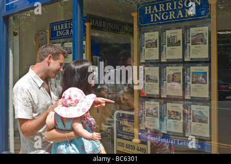 Un jeune couple branché (fin 20's) avec leur bébé à la recherche dans une fenêtre pour agents immobiliers Propriété à louer ou à louer. Banque D'Images